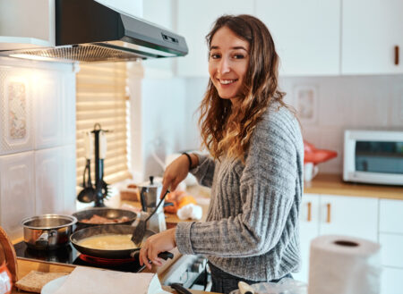 Woman wearing a grey sweater cooks an omelette with a frying pan, she holds a spatula in her left hand.