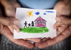 Two pairs of hands hold a child's drawing of a home together. 