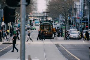 A busy city street in Melbourne with a tram, cars and people crossing the road.
