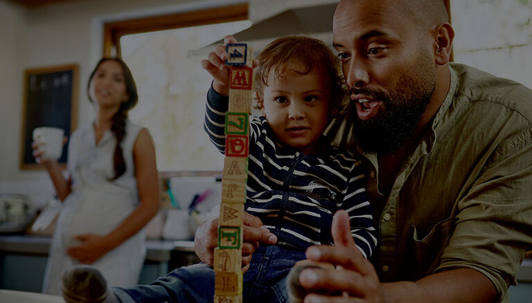 A father helps his child to build a tower of blocks