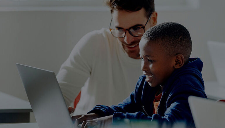 A teacher support a young boy with the computer