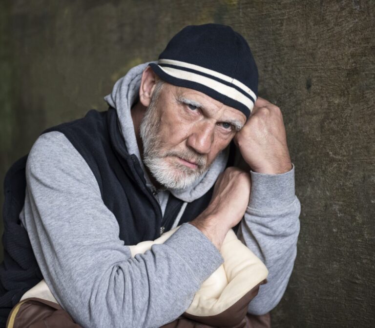 A man wearing a jumper and beanie, and holding a jacket