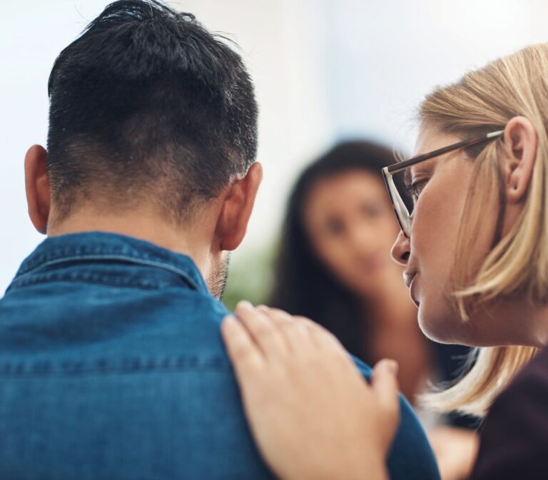 A woman puts her hand on a man's shoulder supportively.
